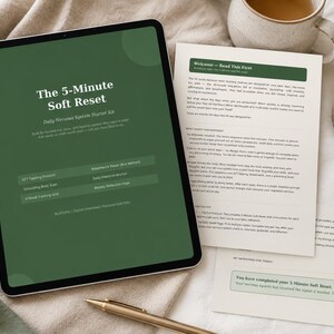 Op de afbeelding: Een digitale tablet toont de tekst "The 5-Minute Soft Reset" op een groene achtergrond. Papieren, een brandende kaars, een pen en een kopje thee completeren de scène, wat wijst op een wellness- of zelfzorgthema.