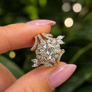 May include: A gold ring featuring a large round brilliant-cut center stone surrounded by a halo of smaller round stones, with additional marquise-cut stones arranged in a leaf-like pattern along the sides of the band and the main setting.