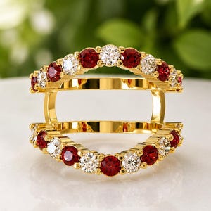 Peut inclure: Une bague double en or composée de deux anneaux parallèles reliés par des barres verticales. Chaque anneau est orné de pierres rondes alternant entre le rouge et le blanc transparent, créant un espace ouvert entre les deux rangées.
