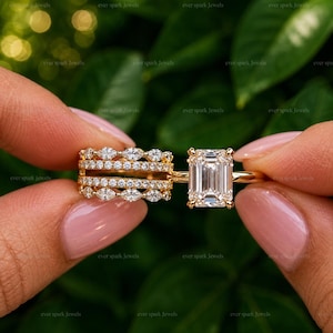 May include: A gold ring set featuring a central emerald-cut stone held by four prongs, flanked by a multi-band design. The bands are adorned with rows of small, clear, round-cut and marquise-cut stones set in a polished gold metal frame.