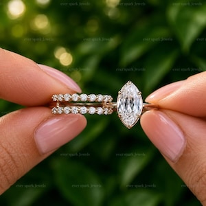 May include: A rose gold ring set featuring a central marquise-cut white gemstone held by prongs, accompanied by a matching band adorned with a row of small round white stones. The metal band has a polished finish and a delicate, slender design.