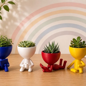 May include: Four colorful human-shaped planters, each holding a different succulent. The planters are blue, white, red, and yellow. The blue planter is reading a book, the white one is holding a cup, the red one is lying down, and the yellow one is sitting.