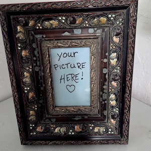 May include: A rectangular picture frame with a dark brown finish and intricate scrollwork detailing. The frame is decorated with small, multicolored embedded accents and features a central insert with the text "your PICTURE HERE!" and a heart symbol.