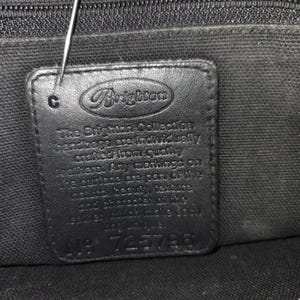 Op de afbeelding: Close-up van een zwart leren label van een Brighton handtas. Het rechthoekige label toont het Brighton-logo en de tekst: "The Brighton Collection handbags are individually crafted..." en "No. 725796".