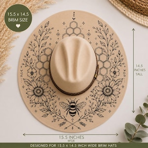 May include: A beige wide-brim hat featuring a black line art design of sunflowers, honeycombs, and a bee. The hat has a brown band and measures 15.5 inches wide by 14.5 inches tall. The brim size is 15.5 by 14.5 inches as indicated by text.