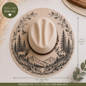 Puede incluir: Un sombrero beige de ala ancha con una ilustración en tinta negra de alces, pinos, montañas y un ave en vuelo. El sombrero tiene una banda marrón oscuro y mide 39,37 cm de ancho por 36,83 cm de alto según las etiquetas visibles.
