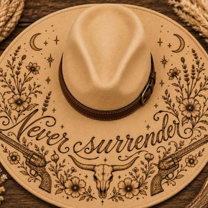 May include: A tan fedora hat with a brown leather band and buckle. The hat's brim features an engraved design with the words "Never Surrender", revolvers, a bull skull, flowers, stars, and crescent moons.