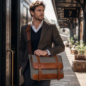 May include: A messenger bag made of grey canvas with brown leather trim, featuring two vertical leather straps with buckles. The bag has an adjustable brown shoulder strap and is worn over a dark brown tweed blazer, a white shirt, and a black vest.