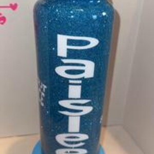 May include: A blue glitter tumbler with a black lid and a white base. The tumbler has the name "Paislee" in white lettering. The text "Shut the fuck up" is also visible on the tumbler.