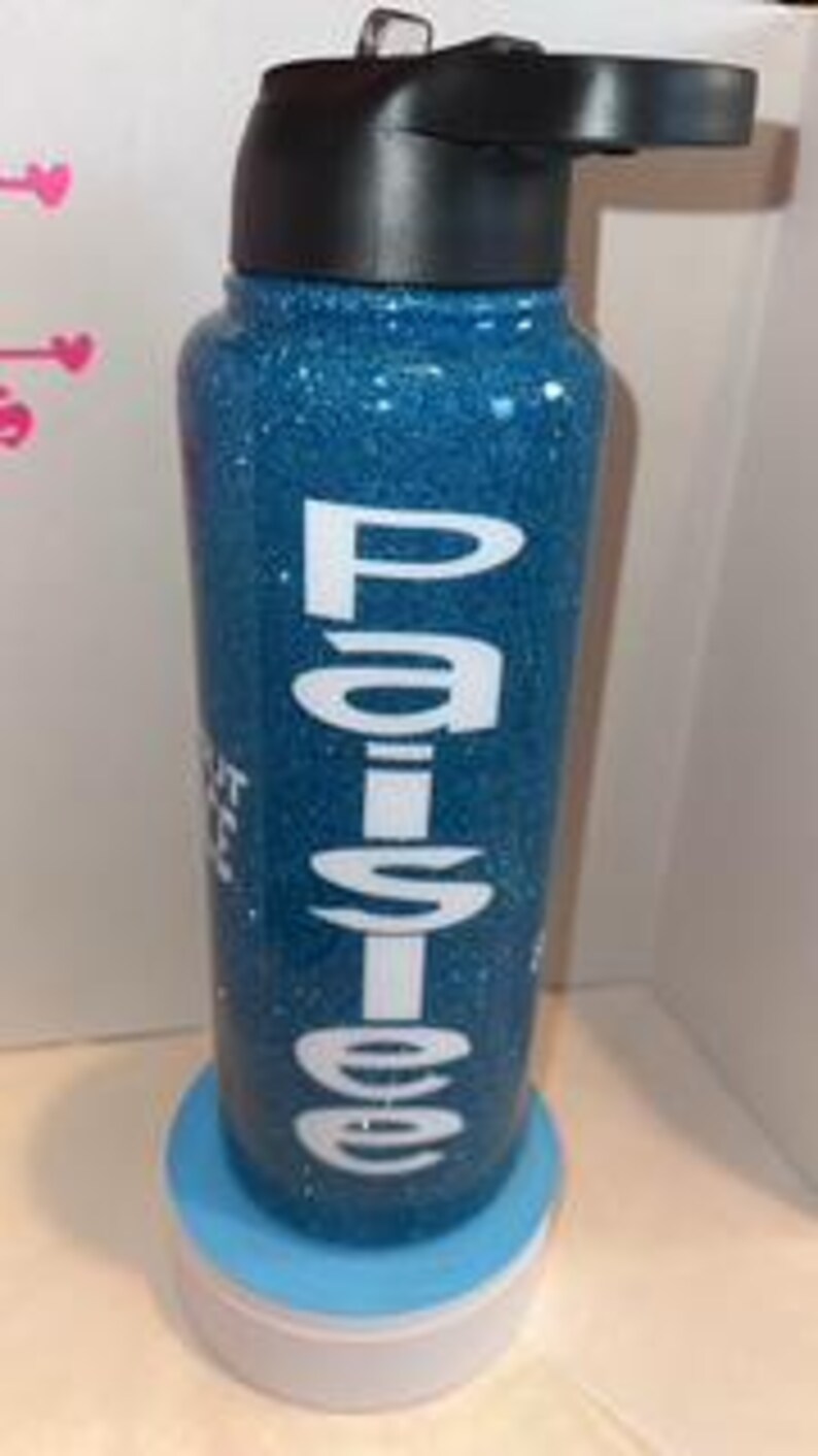 May include: A blue glitter tumbler with a black lid and a white base. The tumbler has the name "Paislee" in white lettering. The text "Shut the fuck up" is also visible on the tumbler.