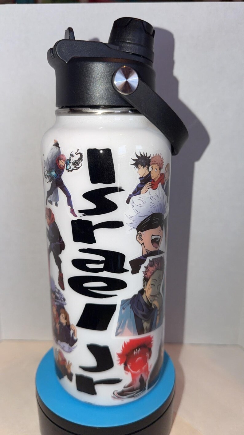 May include: White insulated water bottle featuring anime character illustrations and Japanese text. The bottle has a black lid with a handle and a silver accent. The bottle is on a blue base.