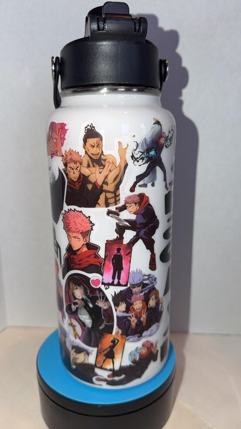 May include: White stainless steel water bottle featuring multiple anime character stickers. The bottle has a black lid and handle. The stickers depict various characters in action poses, with vibrant colors and detailed artwork. The bottle sits on a blue base.