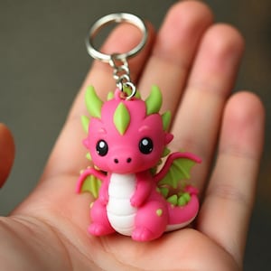 May include: A keychain featuring a small, cartoon-style dragon figurine. The dragon is primarily bright pink with a white belly and light green accents on its horns, back spikes, and wings. It has large black eyes and is attached to a silver metal ring.