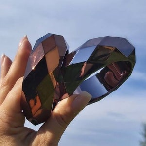 Puede incluir: Dos pulseras rígidas geométricas de color marrón oscuro con un acabado brillante. Las pulseras están apiladas una encima de la otra.