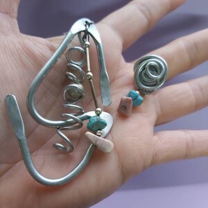 May include: A silver metal earring with a spiral design and turquoise and pink stones.