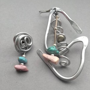 May include: A pair of silver earrings with turquoise and pink stones. The earrings are made of wire and have a unique, abstract design.