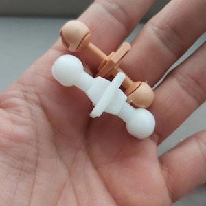 May include: Two doll joint connectors, one white and one beige, with ball-shaped ends. The connectors are designed for attaching doll limbs to the body.