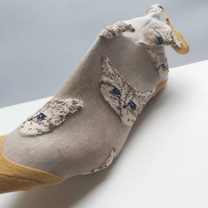 May include: A pair of sheer socks with a yellow trim and a cat face pattern. The socks are made of a thin, delicate fabric and are perfect for adding a touch of whimsy to any outfit.
