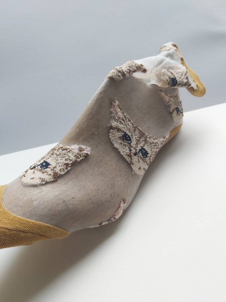 May include: A pair of sheer socks with a yellow trim and a cat face pattern. The socks are made of a thin, delicate fabric and are perfect for adding a touch of whimsy to any outfit.