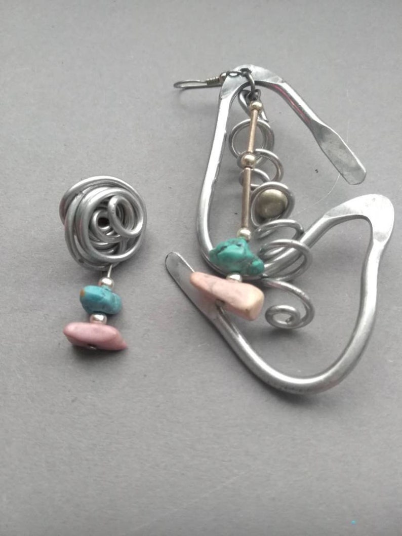 May include: A pair of silver earrings with turquoise and pink stones. The earrings are made of wire and have a unique, abstract design.