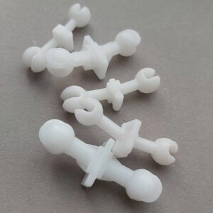 May include: Four white plastic fasteners with different shapes and sizes. The fasteners have a round head and a pointed end.