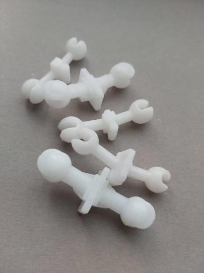 May include: Four white plastic fasteners with different shapes and sizes. The fasteners have a round head and a pointed end.