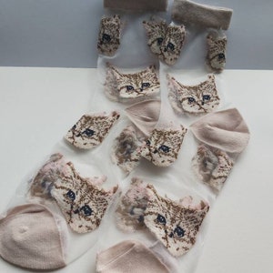 May include: A pair of sheer socks with a cat face pattern. The socks are light pink and have a brown cat face design.