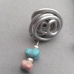 May include: A silver wire wrapped into a spiral shape with two dangling stones, one turquoise and one pink.