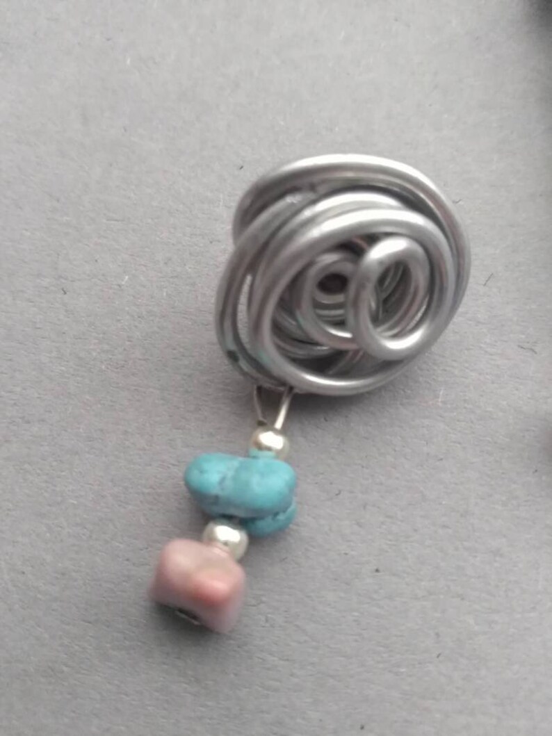 May include: A silver wire wrapped into a spiral shape with two dangling stones, one turquoise and one pink.