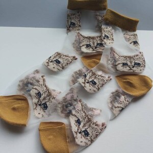 May include: A pair of sheer white socks with a mustard yellow cuff. The socks feature a repeating pattern of brown and white cat faces.