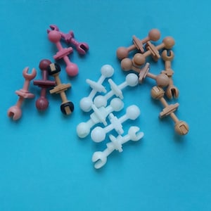 May include: Assortment of plastic toy connectors in white, pink, and brown. The connectors have a ball on one end and a hook on the other end.