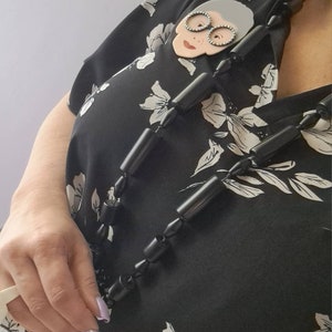 May include: A black and white floral blouse with a black beaded necklace. The necklace features a large, white, cartoon-style face with glasses.