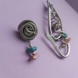 May include: A pair of silver earrings with a spiral design. One earring has a small pink and turquoise bead dangle. The other earring has a larger spiral design with a pink and turquoise bead dangle.