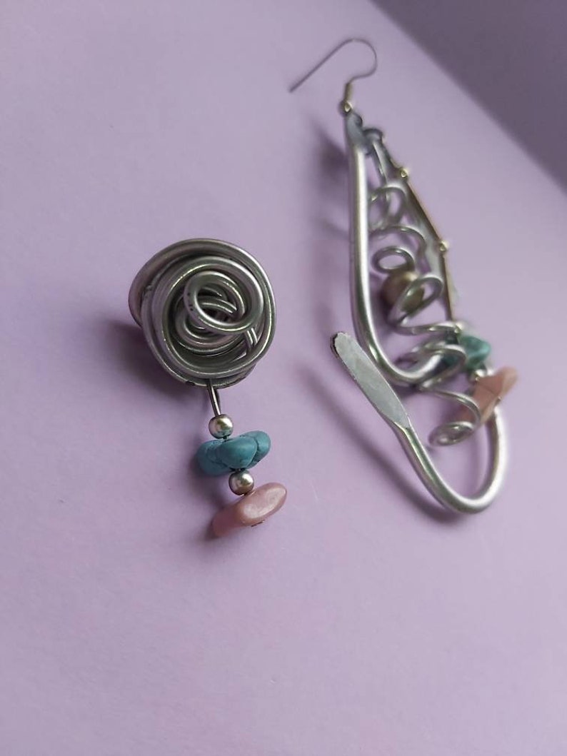 May include: A pair of silver earrings with a spiral design. One earring has a small pink and turquoise bead dangle. The other earring has a larger spiral design with a pink and turquoise bead dangle.