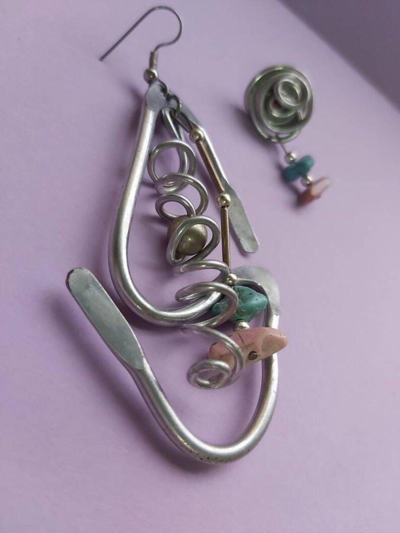 May include: Silver earrings with a spiral design and colorful stones. The earrings are made of metal and have a unique, handmade look.