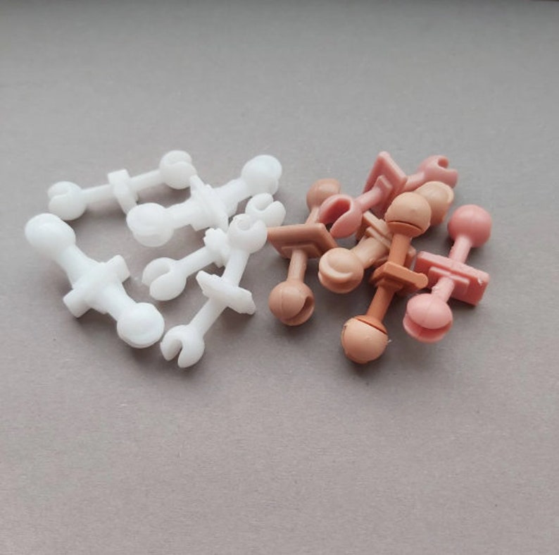 May include: A group of plastic doll parts, some are white and some are a light brown color. The parts are for making a doll's arms and legs.