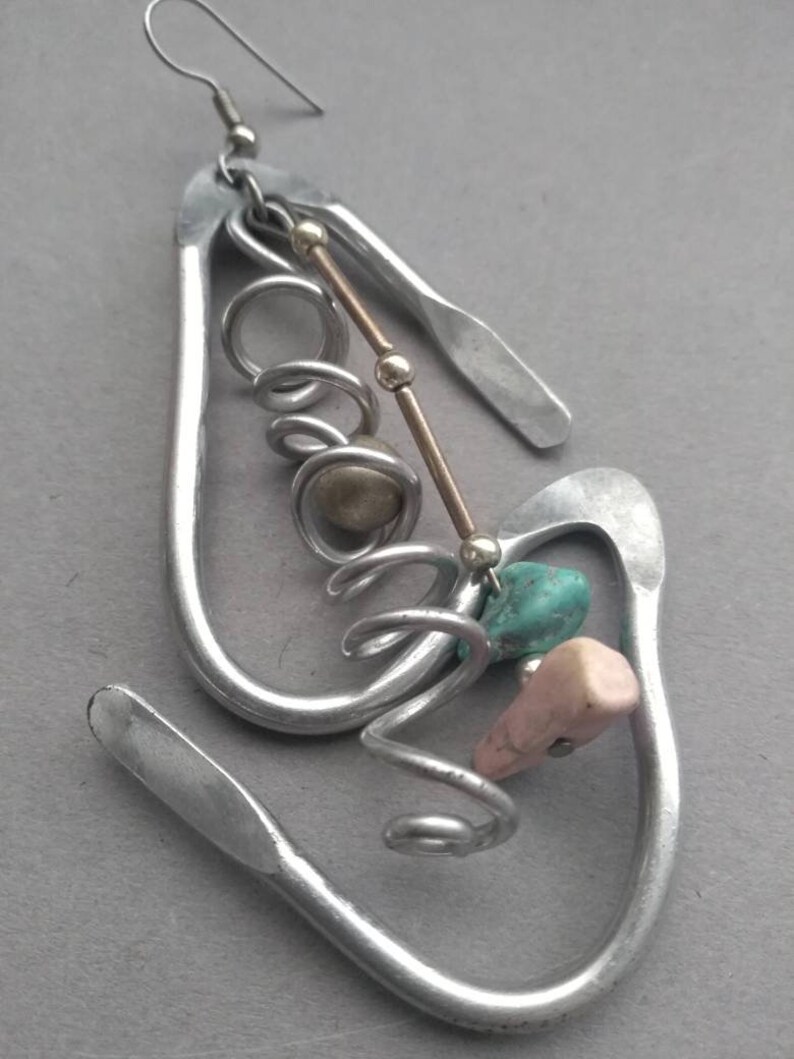 May include: Silver earrings with a unique design featuring a twisted wire, beads, and turquoise and pink stones.