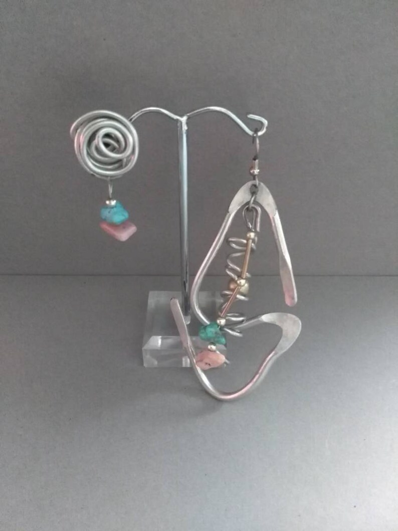 May include: A pair of silver earrings with turquoise and pink stones. The earrings are hanging from a silver stand.
