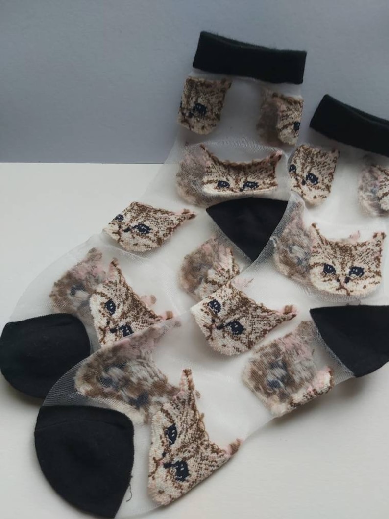 May include: A pair of sheer white socks with a black trim and a repeating pattern of brown cat faces.