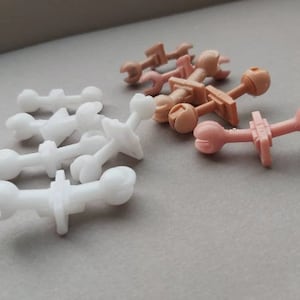 May include: A collection of plastic toy parts in white and brown. The parts are shaped like small figures and have various connectors.