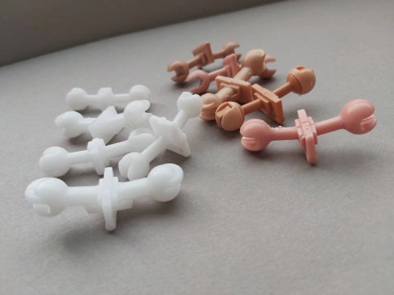 May include: A collection of plastic toy parts in white and brown. The parts are shaped like small figures and have various connectors.