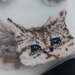 May include: White sheer socks with a brown and white cat face design. The cat face has pink accents and black eyes.