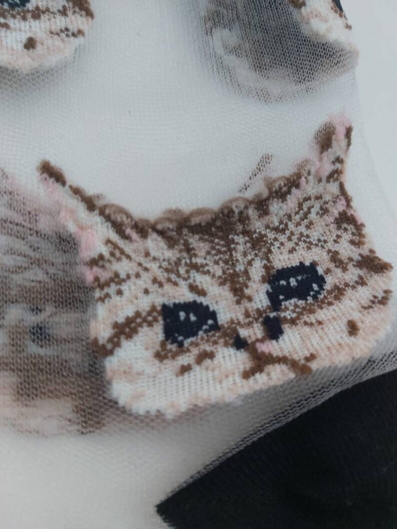 May include: White sheer socks with a brown and white cat face design. The cat face has pink accents and black eyes.