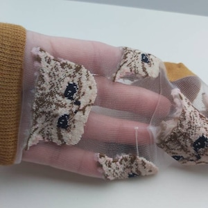 May include: A pair of sheer pink socks with a brown and white cat face pattern. The socks are made of a delicate, lightweight material and feature a subtle shimmer.