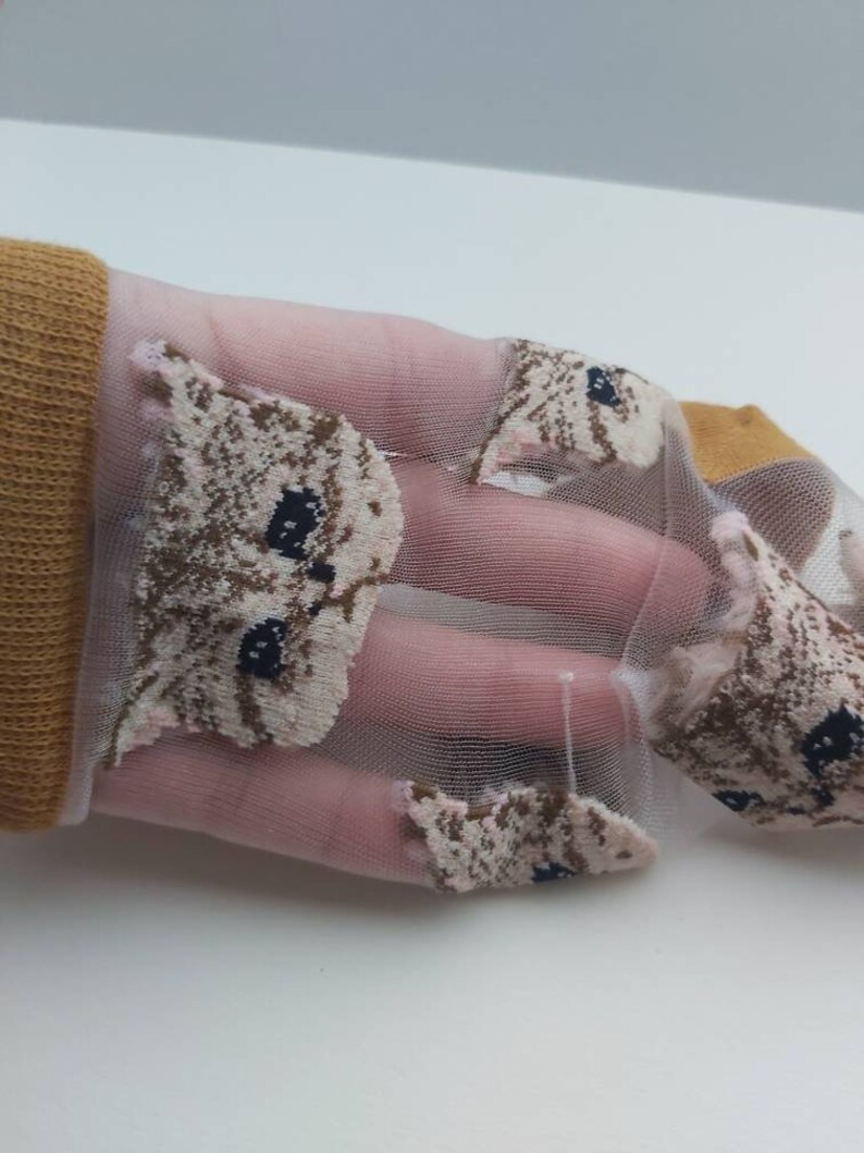 May include: A pair of sheer pink socks with a brown and white cat face pattern. The socks are made of a delicate, lightweight material and feature a subtle shimmer.