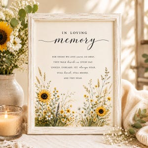May include: A rectangular white distressed wood frame containing a memorial print with the text IN LOVING MEMORY and a poem about those who are missed. The print features a watercolor illustration of yellow sunflowers and wildflowers.