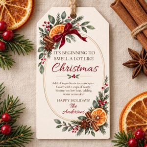 May include: A rectangular cream-coloured gift tag featuring a festive illustration of dried orange slices, cinnamon sticks, star anise, red berries, and pine needles. The text reads: IT'S BEGINNING TO SMELL A LOT LIKE Christmas, instructions, and The Andersons.