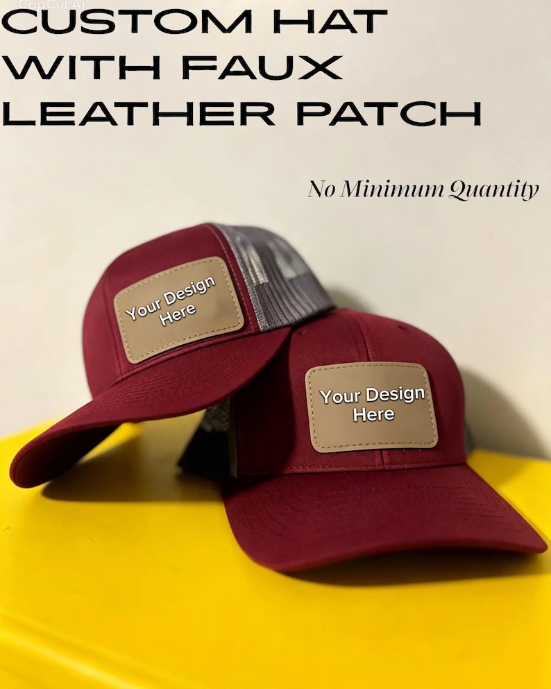 May include: Two maroon trucker hats with grey mesh backs and tan faux leather patches on the front. The patches feature the text "Your Design Here". The image includes the text "CUSTOM HAT WITH FAUX LEATHER PATCH" and "No Minimum Quantity".