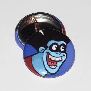 May include: A blue and red button with a cartoon image of a blue character with a black mask and a wide smile. The character has a black and white striped hair.
