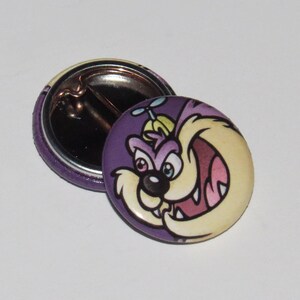 May include: Purple and yellow cartoon character button with a white background. The character has a large, toothy grin and a propeller on its head.